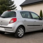 Renault Clio 3 grise garée dans une allée pavée devant une maison.